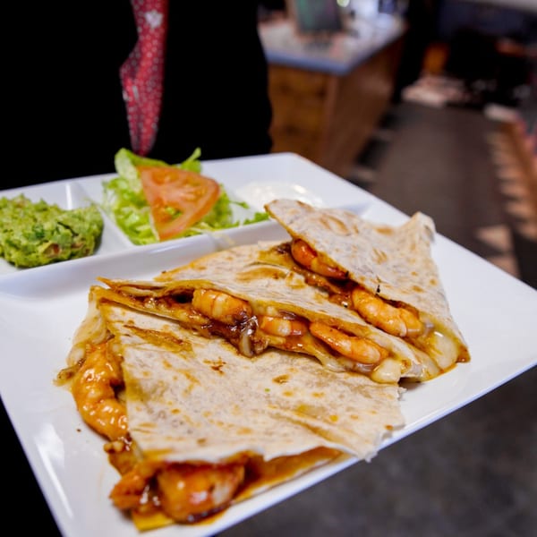 Shrimp quesadillas with melted cheese, served with guacamole, lettuce, tomato, and sour cream.