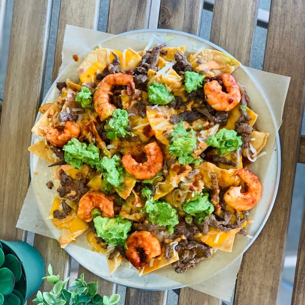 Overhead view of The Taco Shop's nachos with shrimp, steak, guacamole, and cheese on a wooden table.