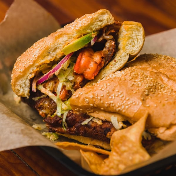 A large Mexican torta sandwich with shrimp, avocado, red onion, and shredded lettuce.