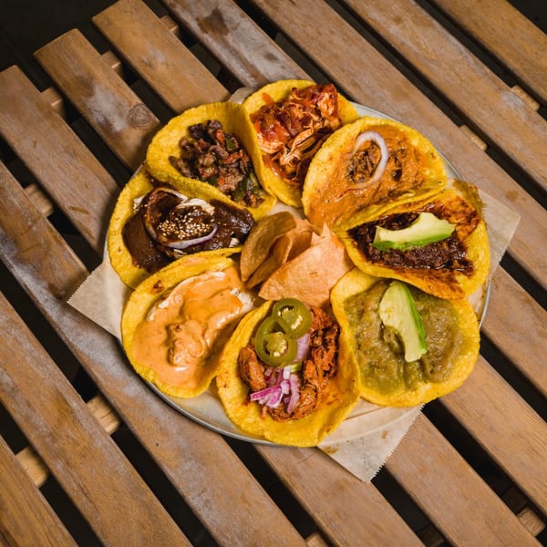 A platter of diverse Mexican tacos, including mole, al pastor, and carne asada, on a wooden table.