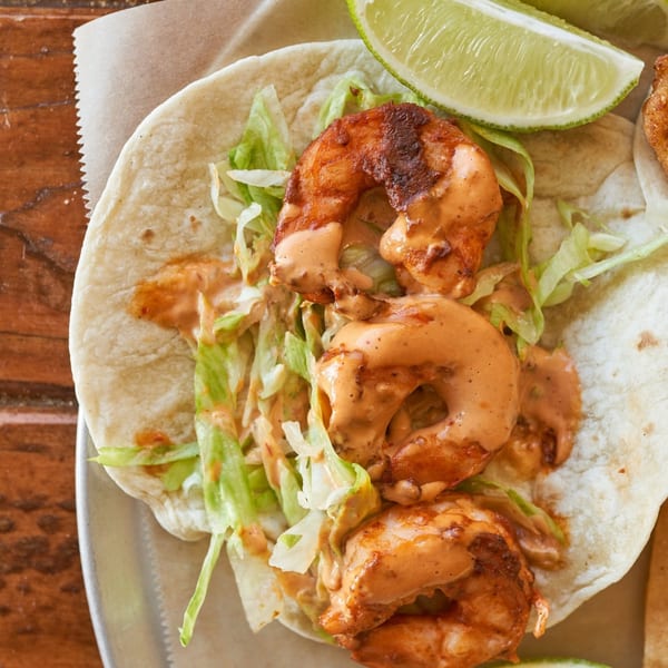 Close-up of a shrimp taco with shredded lettuce, creamy sauce, and a lime wedge.